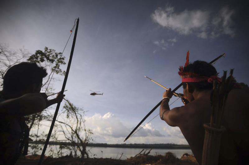 Indigenous people point their bows and arrows at a police helicopter