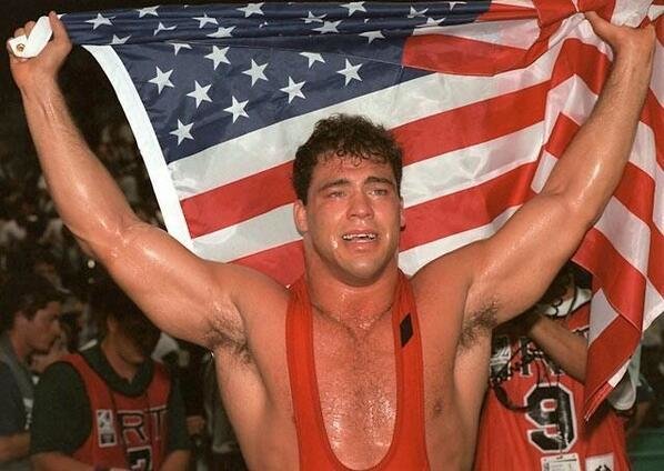 Wrestler Kurt Angle holds up the American Flag after winning gold in the 1996 Olympics with a broken