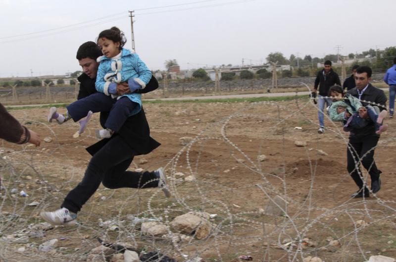 Syrians jump over barbed wire as they flee from the Syrian town of Ras al-Ain to the Turkish border
