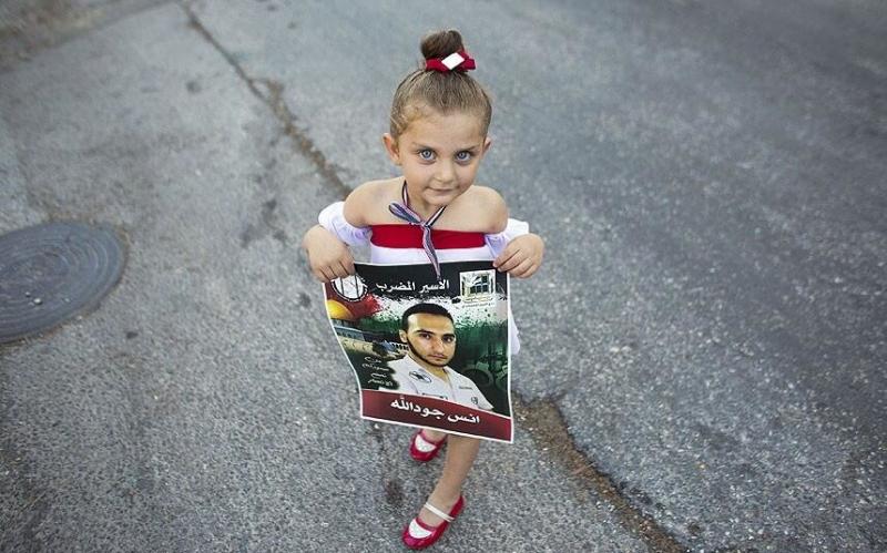 صورة ‏طفلة تحمل صورة لاحد المعتقلين في مظاهرة خارج مبنى الصليب الأحمر في القدس دعما للأسرى الفلسطينيين المضربين عن الطعام